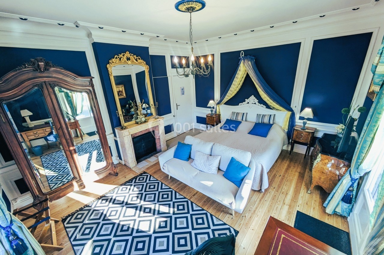 Chambre élégante avec murs bleu foncé, lit double, cheminée, armoire en bois et tapis à motifs géométriques.