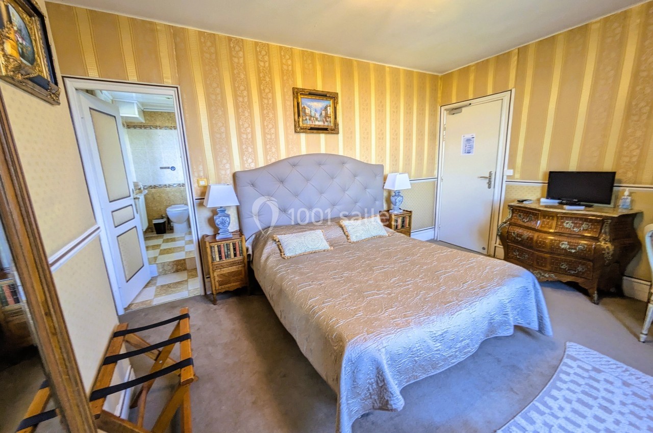 Chambre avec lit double, mobilier classique, téléviseur, et accès à une salle de bain attenante.