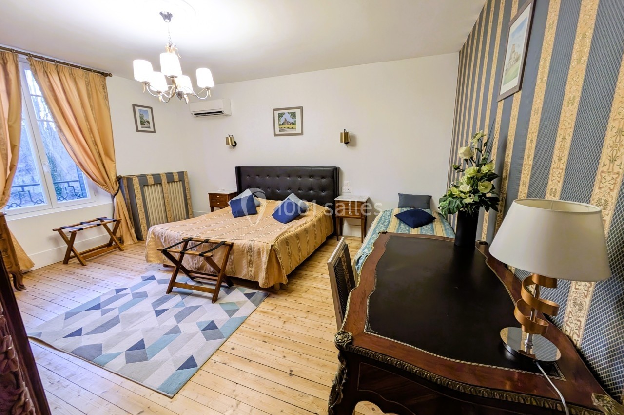 Chambre lumineuse avec lit double, bureau en bois, rideaux dorés et parquet clair, décorée dans un style classique.
