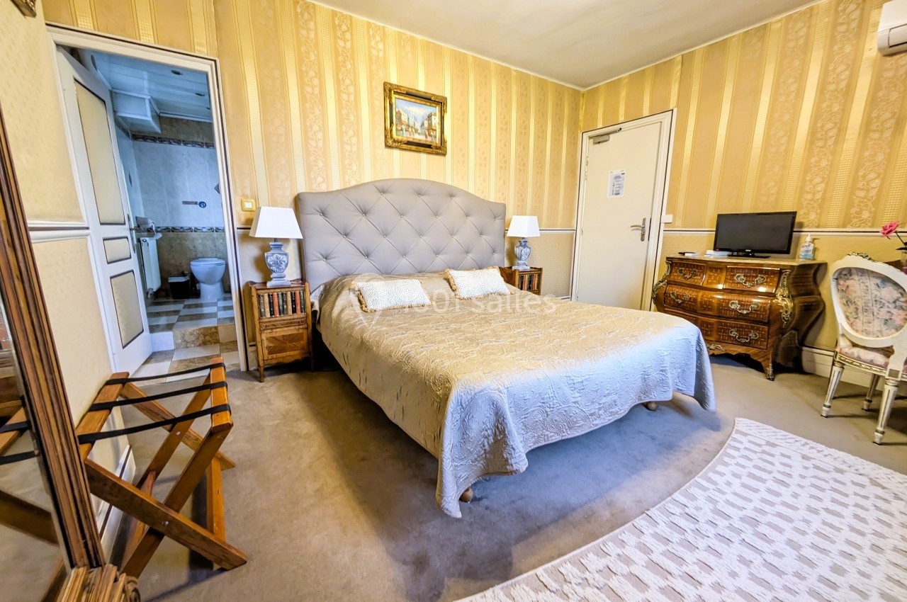 Chambre avec lit double, mobilier classique, murs à rayures jaunes, salle de bain attenante et petite télévision.