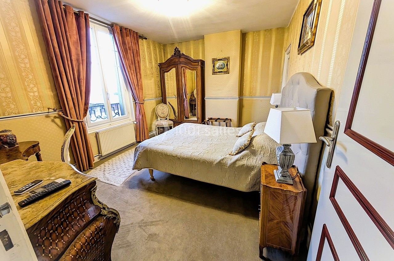 Chambre classique avec lit double, armoire en bois, tapis beige, rideaux épais et lumière naturelle provenant d'une fenêtre.