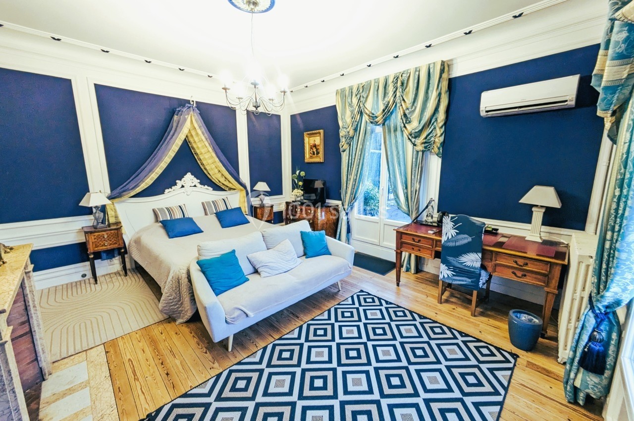 Chambre élégante avec murs bleus, lit double, mobilier en bois, tapis géométrique et fenêtre avec rideaux.