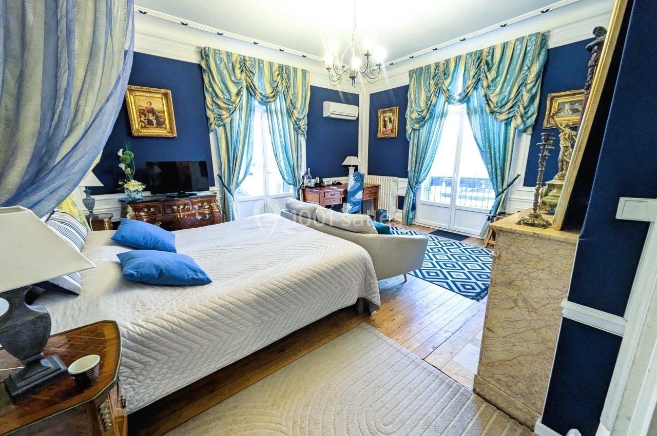 Chambre élégante avec murs bleus, lit double, rideaux assortis, cheminée en marbre et mobilier classique.