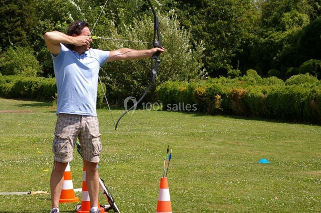 Un homme tire à l'arc dans un parc, entouré de cônes de signalisation et de verdure.