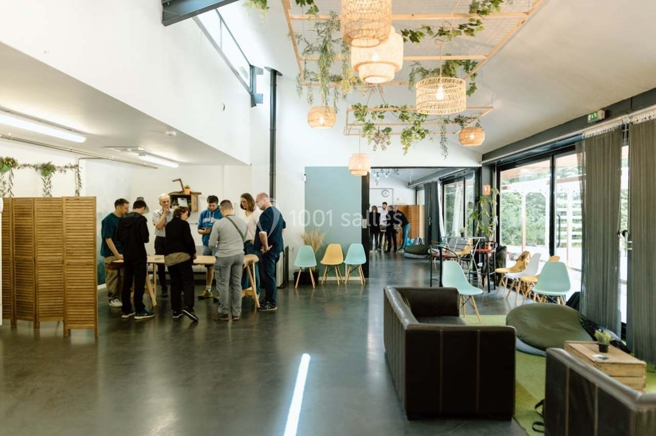 Un groupe de personnes échange dans un espace de coworking lumineux avec mobilier moderne et plantes suspendues.
