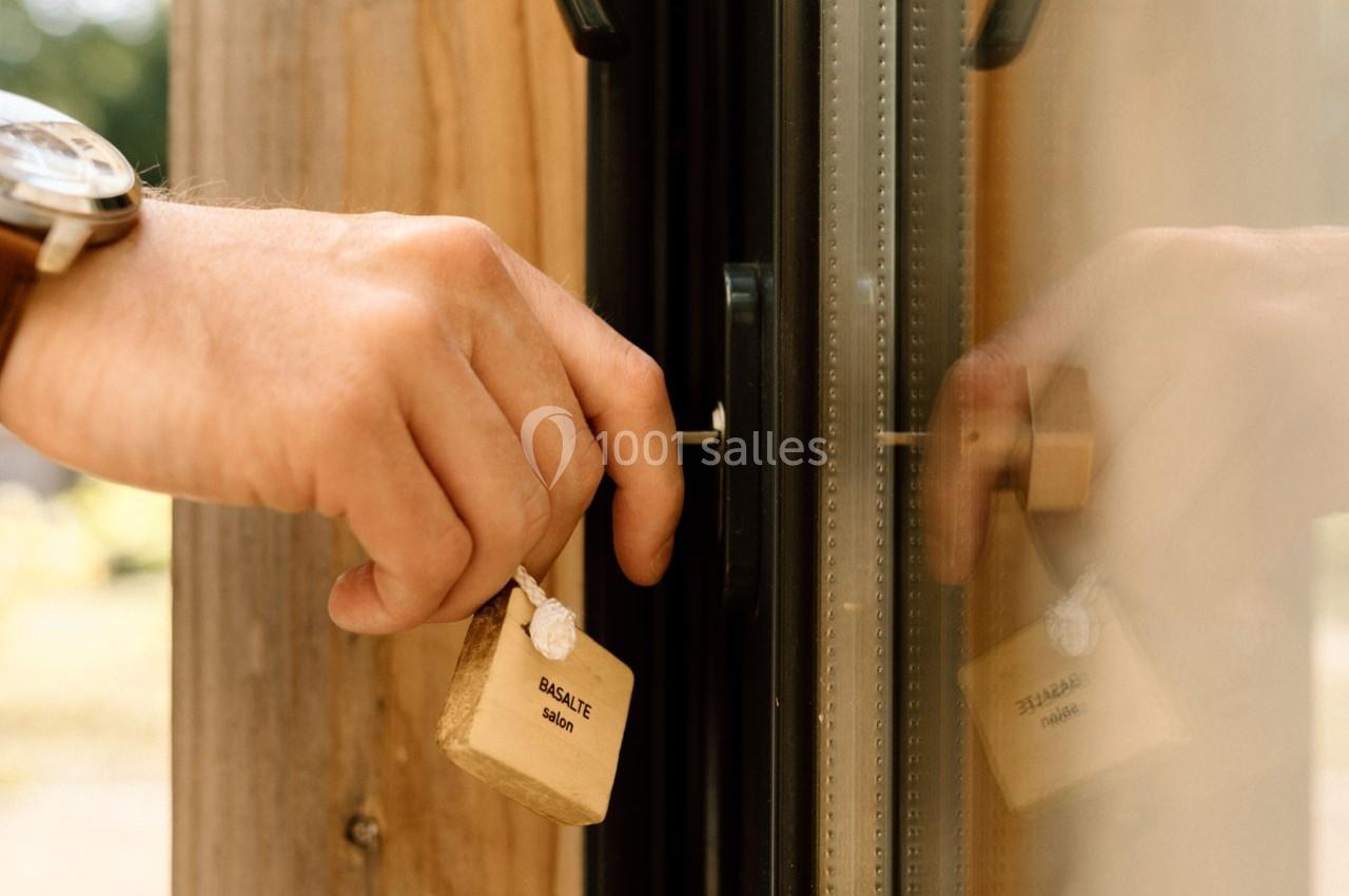 Main verrouillant une porte en verre avec un cadenas beige marqué ’ÉGALITÉ’.