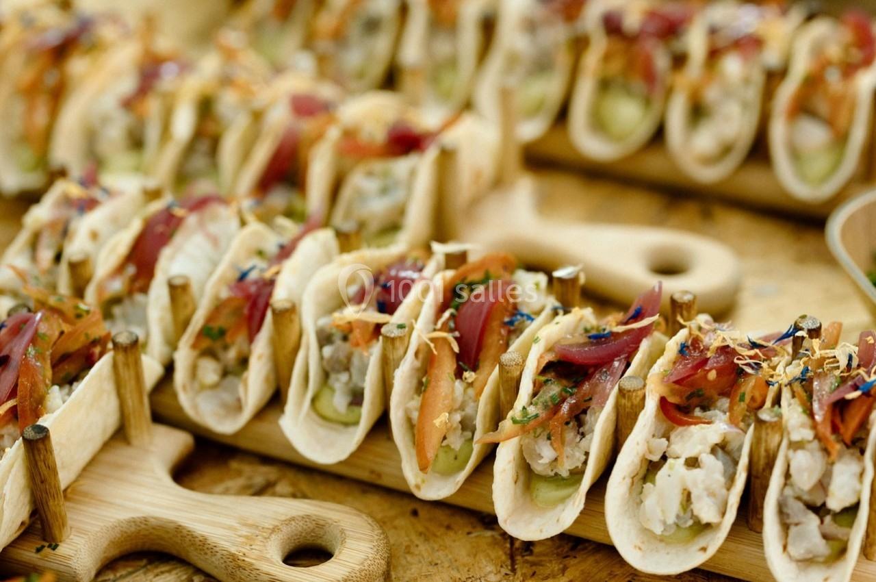 Plateau de mini-tacos garnis de légumes, herbes fraîches et morceaux de viande, présentés sur des planches en bois.