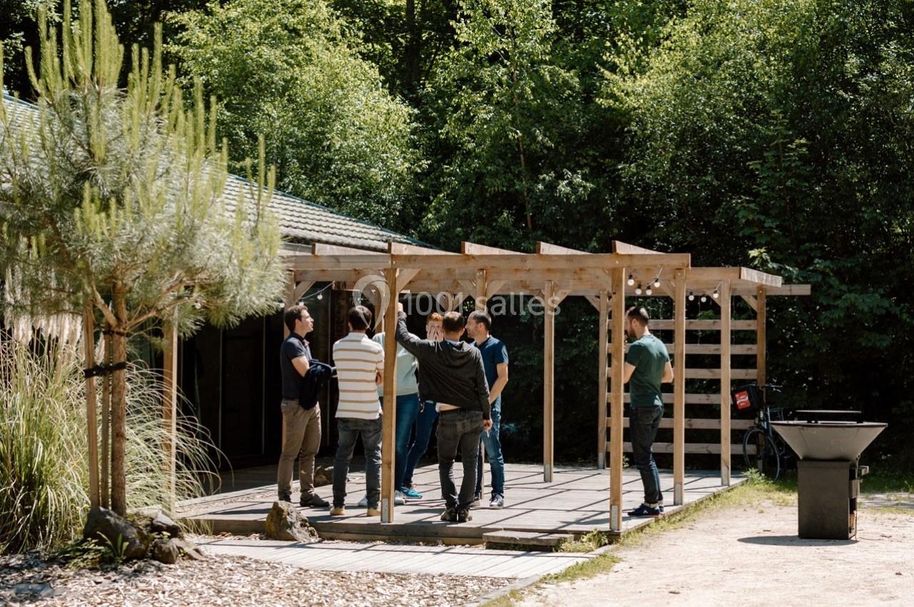 Un groupe de personnes discute sous une pergola en bois dans un environnement naturel et ensoleillé.