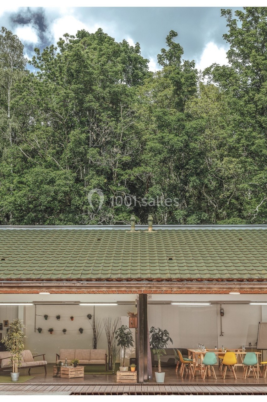 Espace intérieur lumineux avec mobilier moderne et ouvert sur une terrasse, entouré de végétation dense.