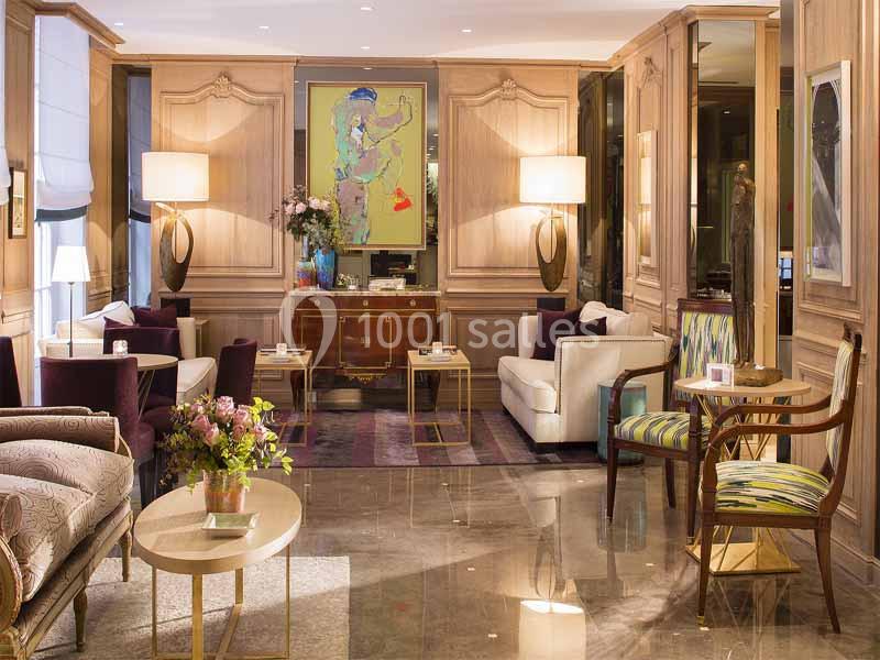 Salon élégant avec mobilier classique, fauteuils colorés, tables basses, éclairage doux et tableau moderne au mur.