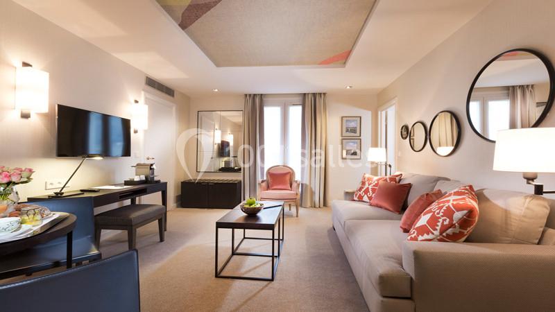 Salon lumineux avec canapé, fauteuil, table basse, télévision murale, bureau et décoration moderne.