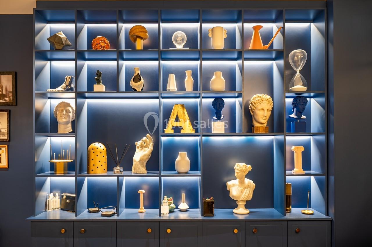 Étagère bleue éclairée présentant des objets décoratifs variés, dont des sculptures, vases et accessoires design.