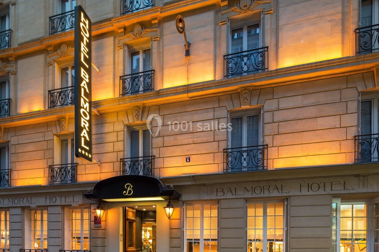 Façade d'un hôtel parisien éclairé, avec enseigne lumineuse ’Hotel Balmoral’ et balcons en fer forgé.