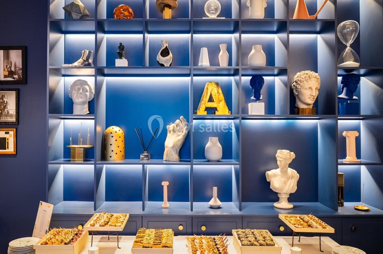 Étagère bleue avec objets décoratifs variés en arrière-plan et buffet de bouchées apéritives sur une table blanche.