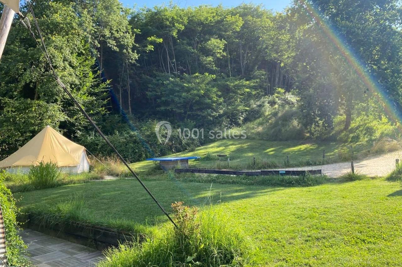 Tente beige installée dans un espace verdoyant avec pelouse, arbres et lumière naturelle sous un ciel dégagé.
