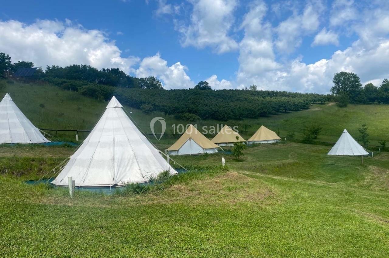 Tentes blanches et beiges installées sur une prairie verdoyante sous un ciel partiellement nuageux.