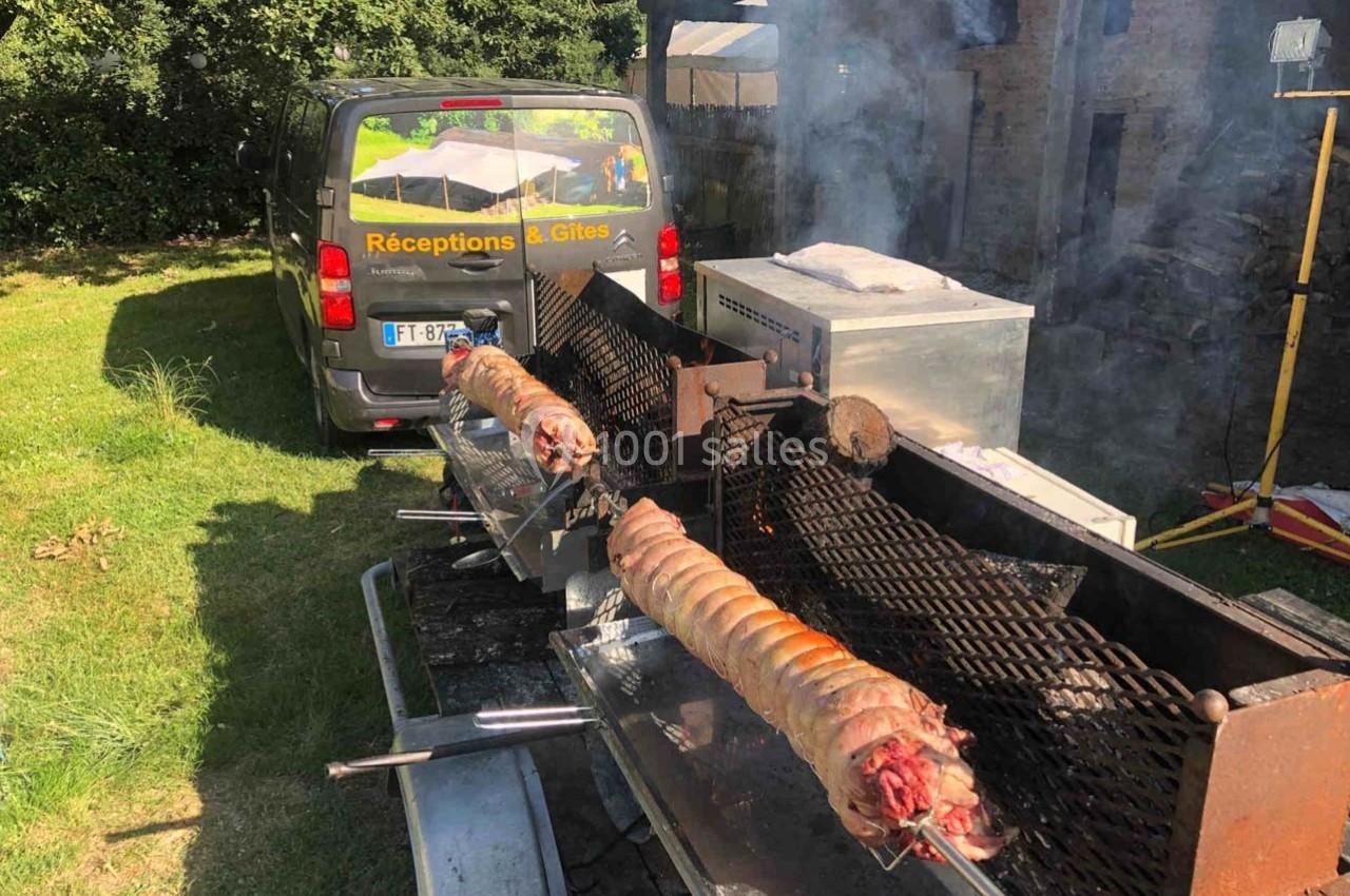 Deux porcelets rôtissent sur des broches devant un véhicule utilitaire marqué ’Réceptions & Gîtes’.
