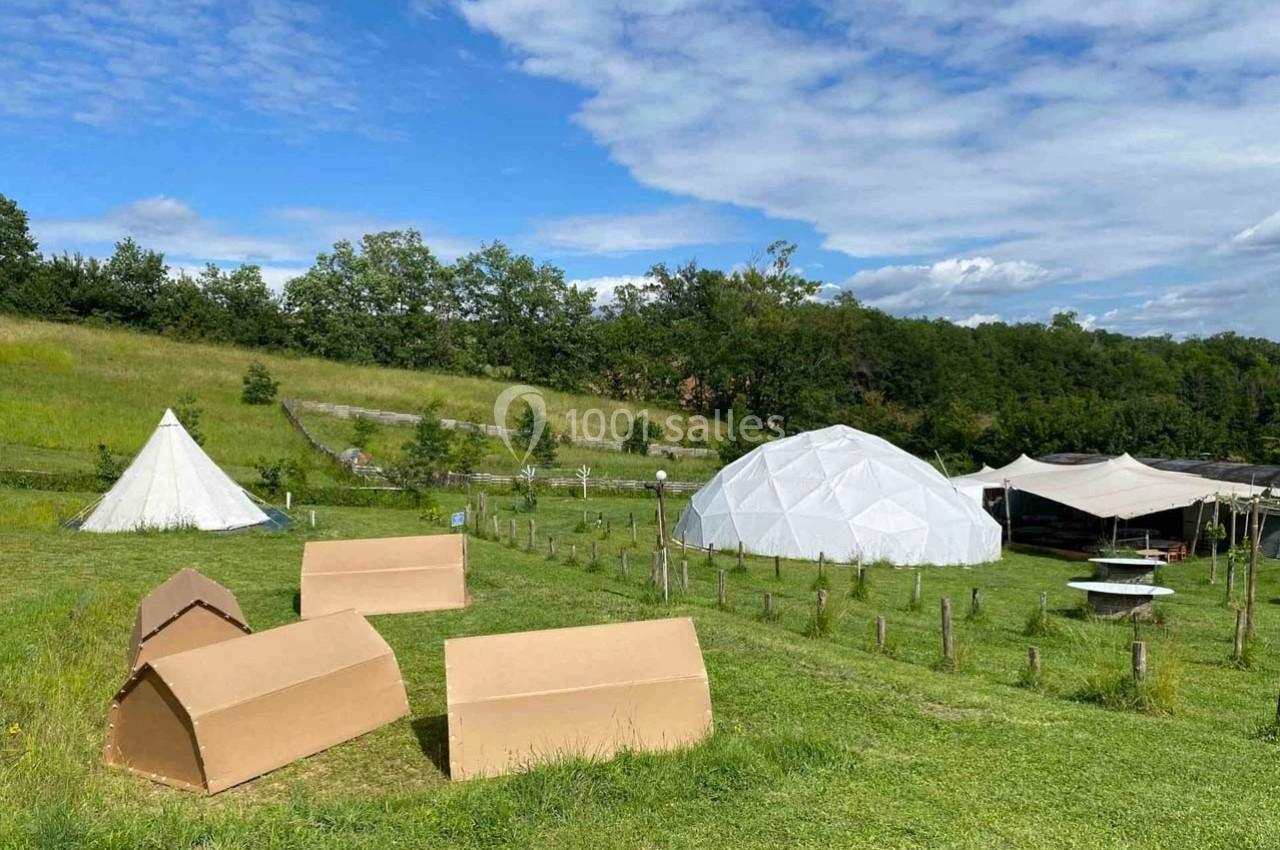 Un terrain verdoyant avec des tentes, un dôme géodésique blanc et des structures en bois sous un ciel dégagé.