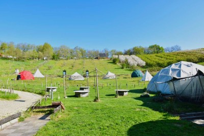 Intérieur d'une tente avec matelas, coffre noir, tapis coloré et vue partielle sur un paysage extérieur.
