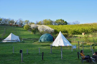 Intérieur d'une tente avec matelas, coffre noir, tapis coloré et vue partielle sur un paysage extérieur.
