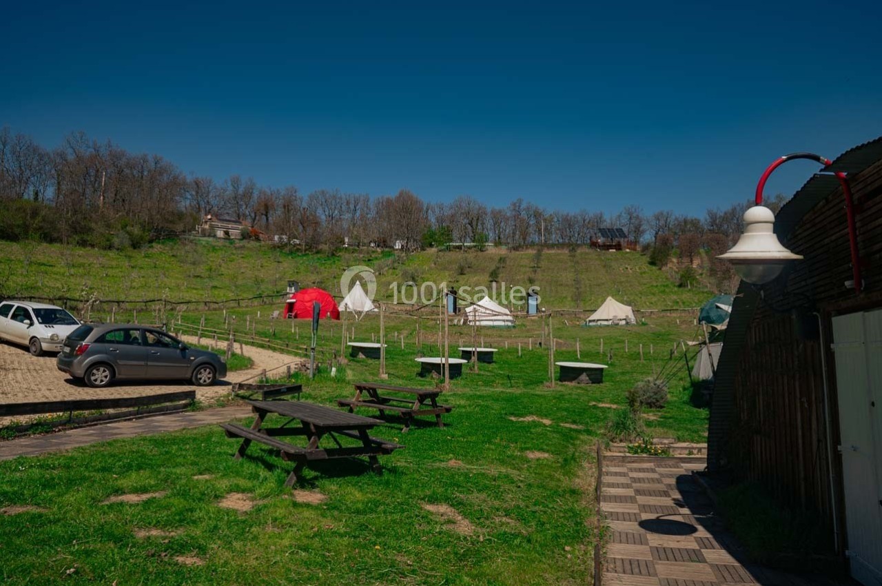 Vue d'un espace extérieur avec tables de pique-nique, tentes, vignes en arrière-plan et un lampadaire au premier plan.