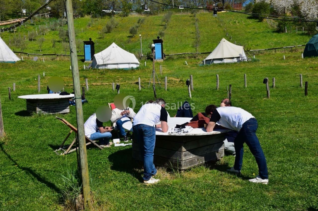 Des personnes travaillent en groupe autour de tables en extérieur, dans un cadre verdoyant avec des tentes en arrière-plan.