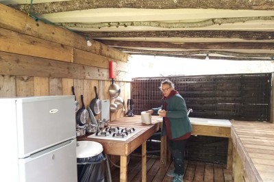 Intérieur d'une tente avec matelas, coffre noir, tapis coloré et vue partielle sur un paysage extérieur.