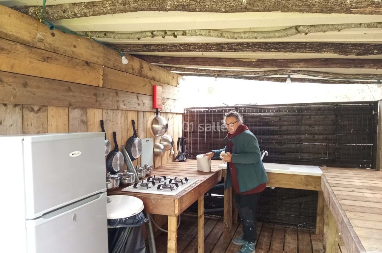 Une personne prépare quelque chose dans une cuisine extérieure en bois avec un évier, un réfrigérateur et des ustensiles…