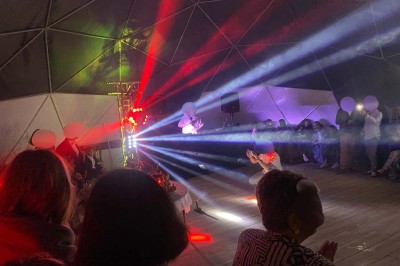 Intérieur d'une tente avec matelas, coffre noir, tapis coloré et vue partielle sur un paysage extérieur.