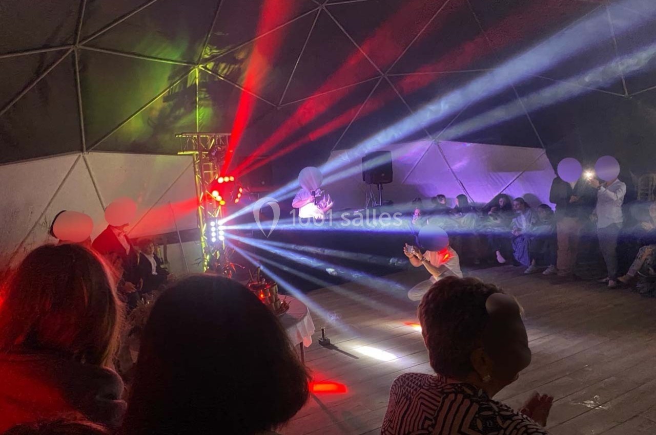 Personnes assises et debout dans un dôme éclairé par des faisceaux lumineux colorés lors d'un événement.