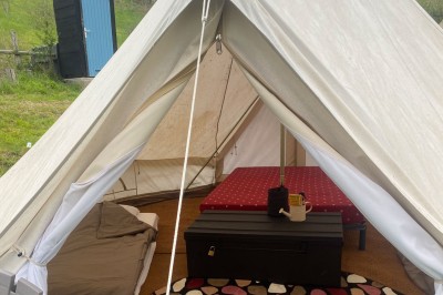 Intérieur d'une tente avec matelas, coffre noir, tapis coloré et vue partielle sur un paysage extérieur.