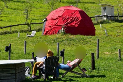 Intérieur d'une tente avec matelas, coffre noir, tapis coloré et vue partielle sur un paysage extérieur.
