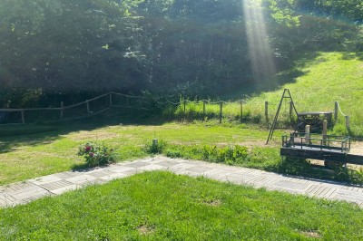 Salle commune avec tables, chaises, télévision murale, meubles en bois et sol carrelé, éclairée par des plafonniers.