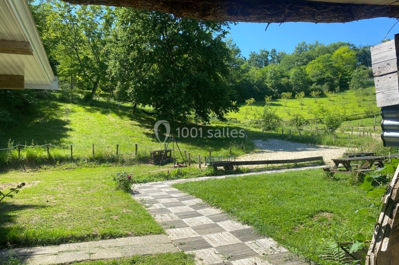Vue d'un jardin verdoyant avec une allée pavée, des arbres et une clôture en arrière-plan sous un ciel ensoleillé.