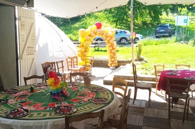 Salle commune avec tables, chaises, télévision murale, meubles en bois et sol carrelé, éclairée par des plafonniers.