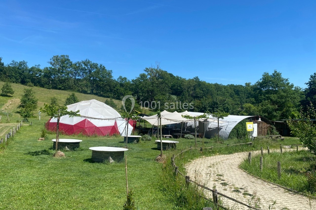 Deux grandes tentes et des tables en plein air dans un espace vert entouré d'arbres et de collines.