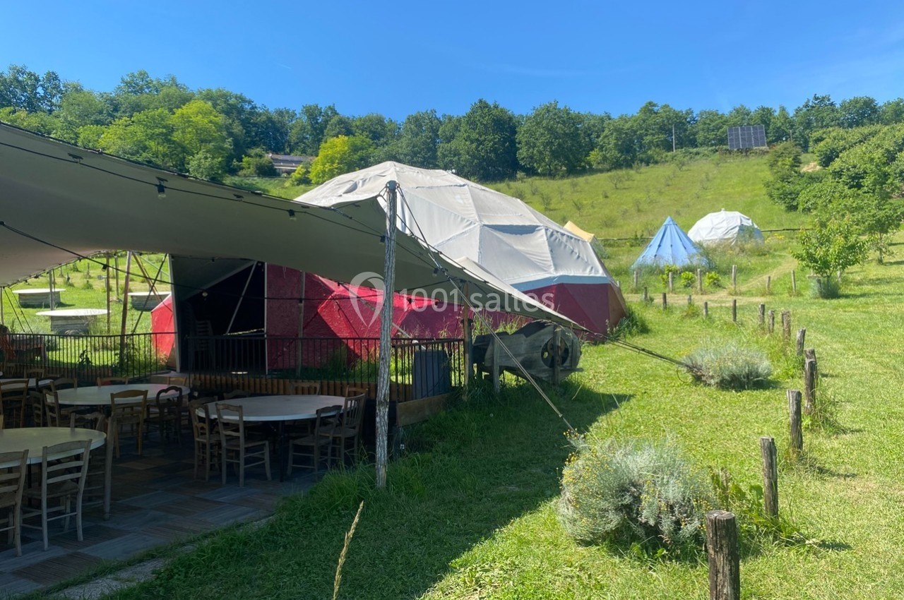 Tentes géodésiques et espace extérieur aménagé avec tables et chaises, entourés de verdure et collines boisées.