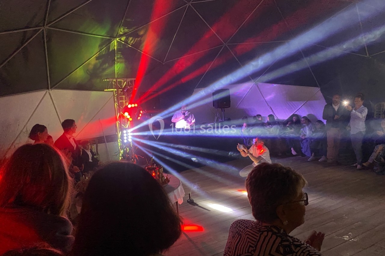 Personnes rassemblées dans une structure géodésique, observant un spectacle lumineux avec faisceaux colorés.