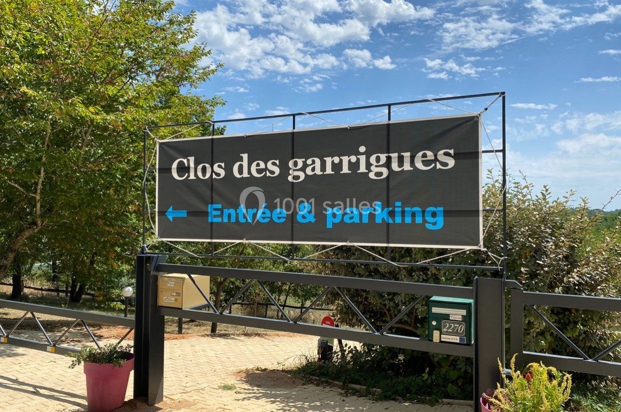 Panneau indiquant ’Clos des garrigues’ avec flèche vers l'entrée et le parking, situé devant une grille métallique.