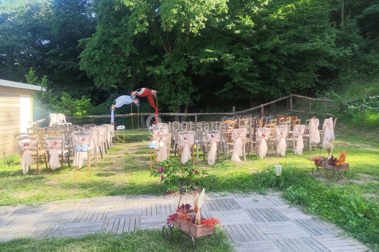 Chaises décorées disposées en extérieur pour une cérémonie, avec une arche ornée de tissu devant un espace boisé.