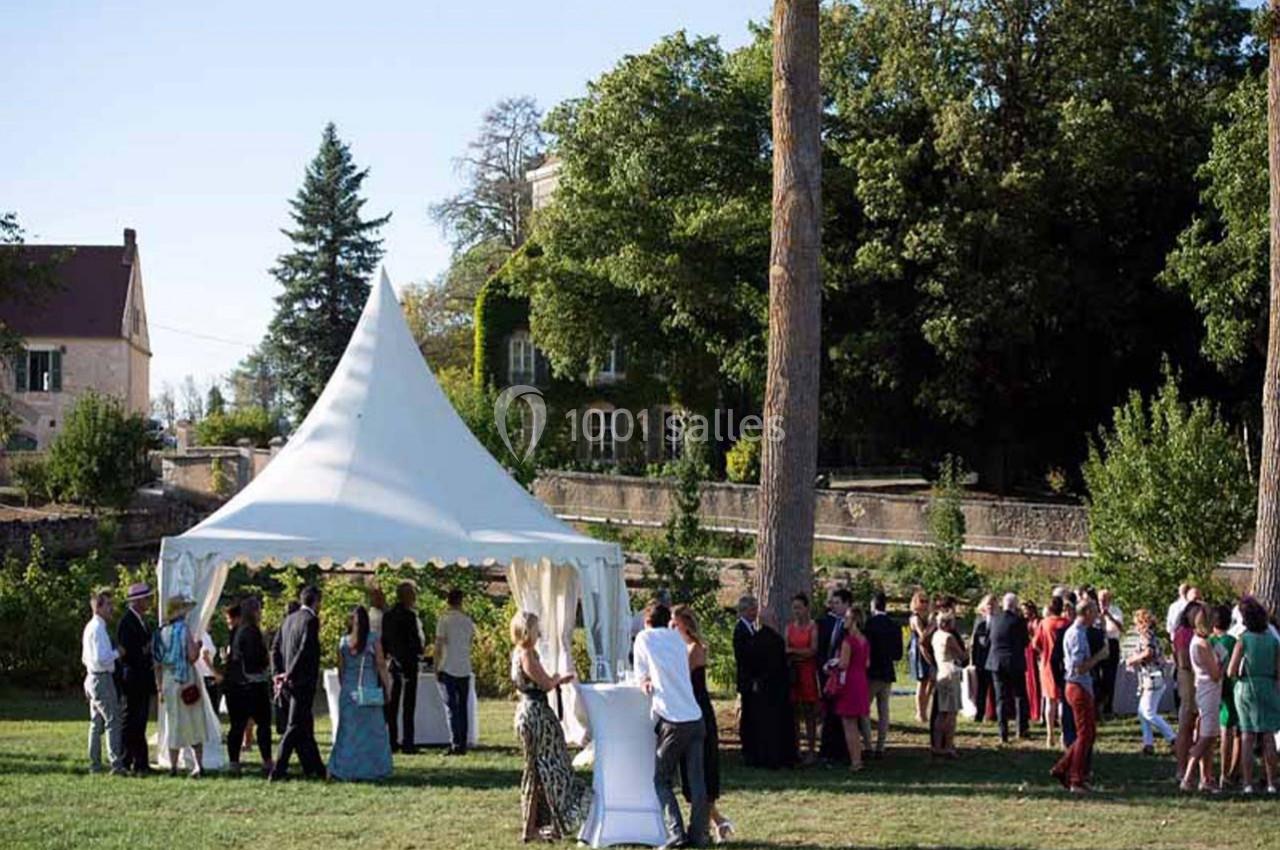 Groupe de personnes rassemblées autour d'une tente blanche dans un jardin verdoyant par une journée ensoleillée.
