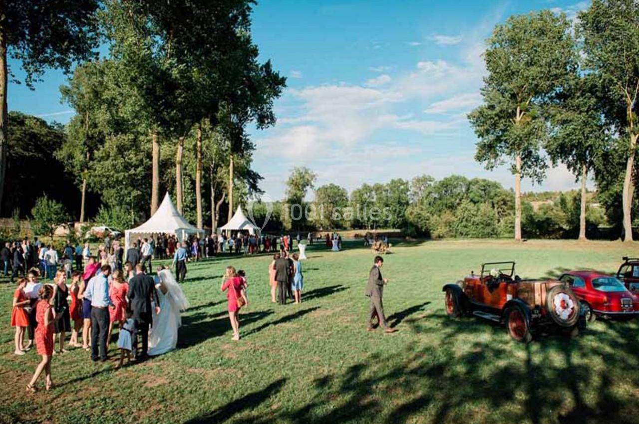 Groupe de personnes rassemblées dans un parc pour un événement, avec des tentes blanches et une voiture ancienne.