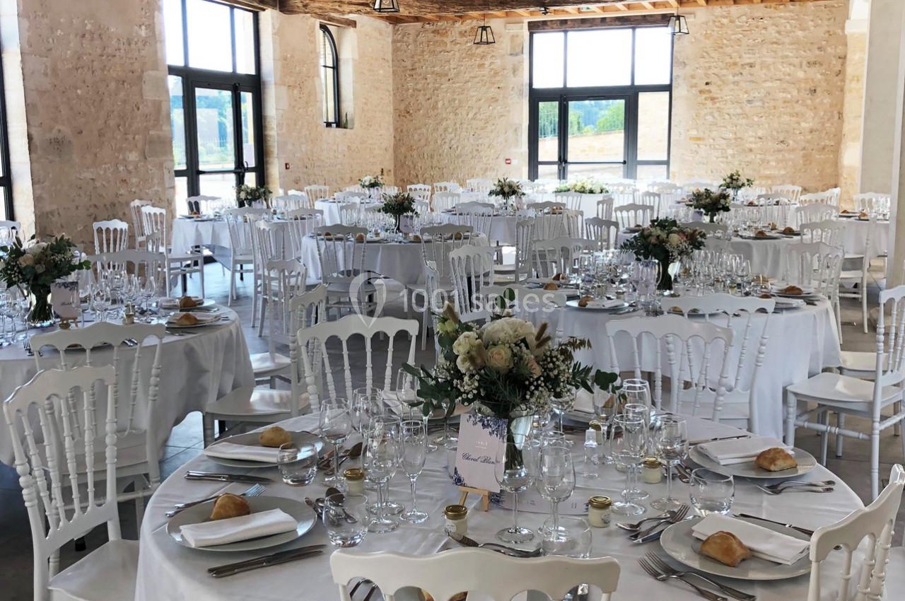 Salle de réception lumineuse avec tables rondes dressées, décorées de fleurs et couverts élégants.