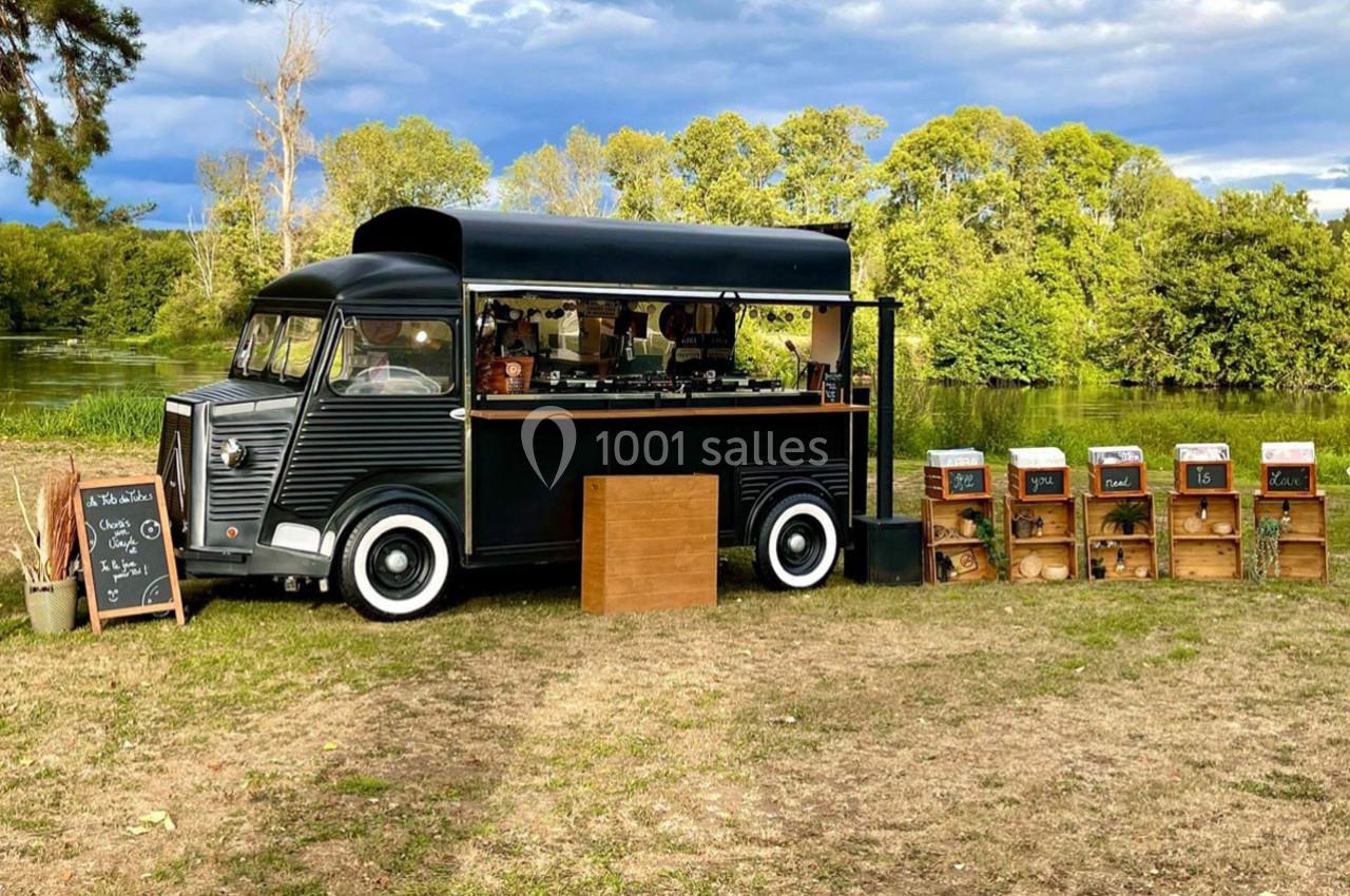 Camion noir aménagé en café ambulant, entouré de caisses en bois et situé dans un cadre naturel verdoyant.