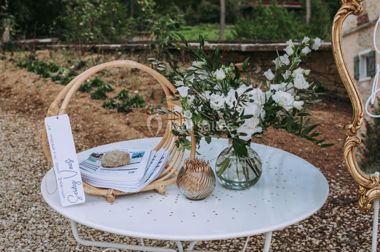 Un bouquet de fleurs blanches dans un vase en verre et des brochures sur une table ronde blanche en extérieur.
