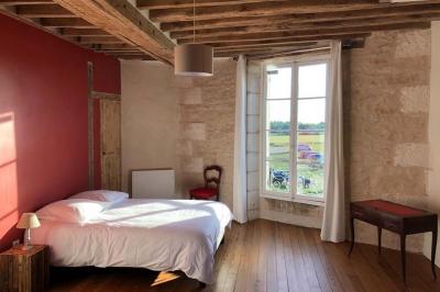 Chambre lumineuse avec un lit double, murs en pierre et peinture bleue, parquet en bois et fenêtre donnant sur la campagne.