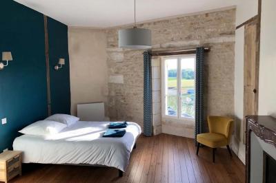 Chambre lumineuse avec un lit double, murs en pierre et peinture bleue, parquet en bois et fenêtre donnant sur la campagne.