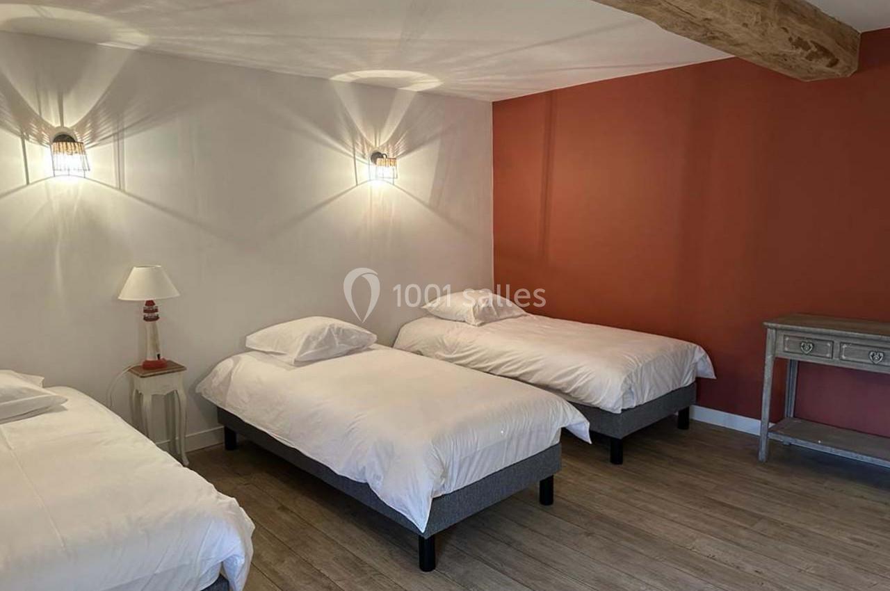 Trois lits simples avec draps blancs dans une chambre à la décoration sobre, mur orange et poutre apparente.