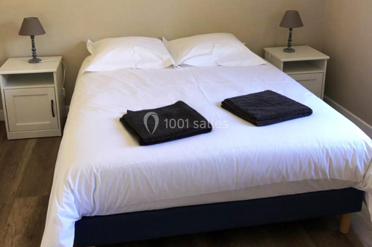 Lit double avec draps blancs, deux serviettes pliées au pied, tables de chevet avec lampes dans une chambre lumineuse.