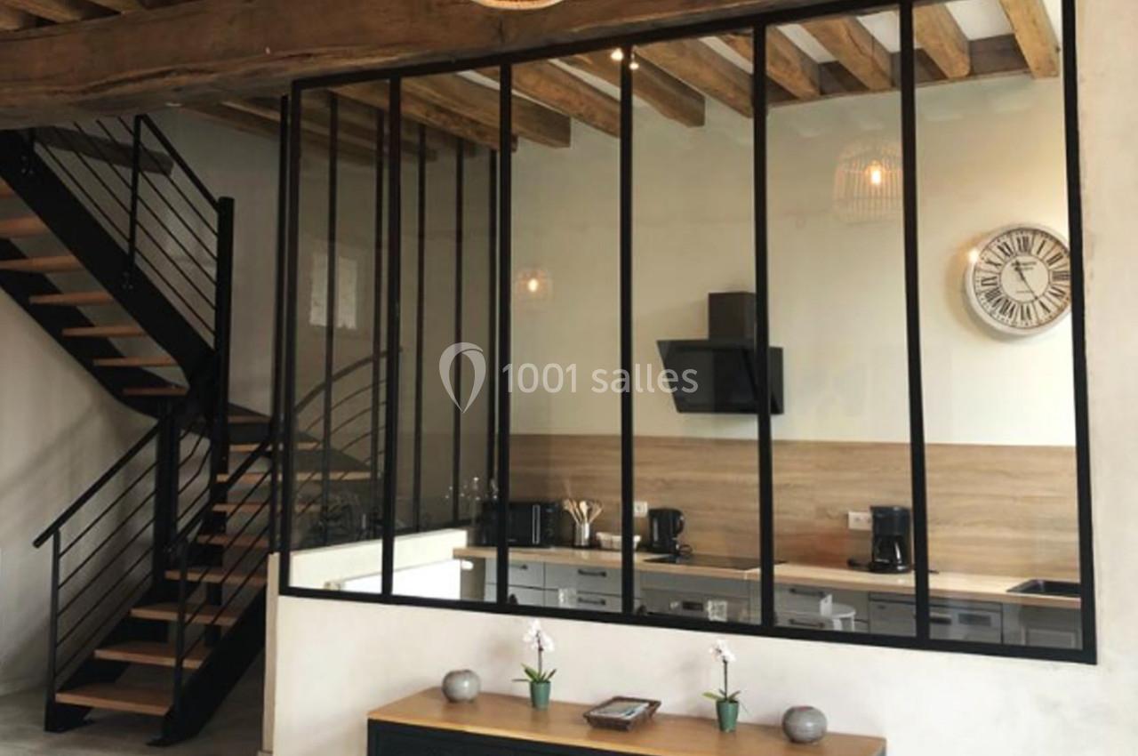 Cuisine moderne avec verrière noire, poutres apparentes, escalier métallique et décoration minimaliste.